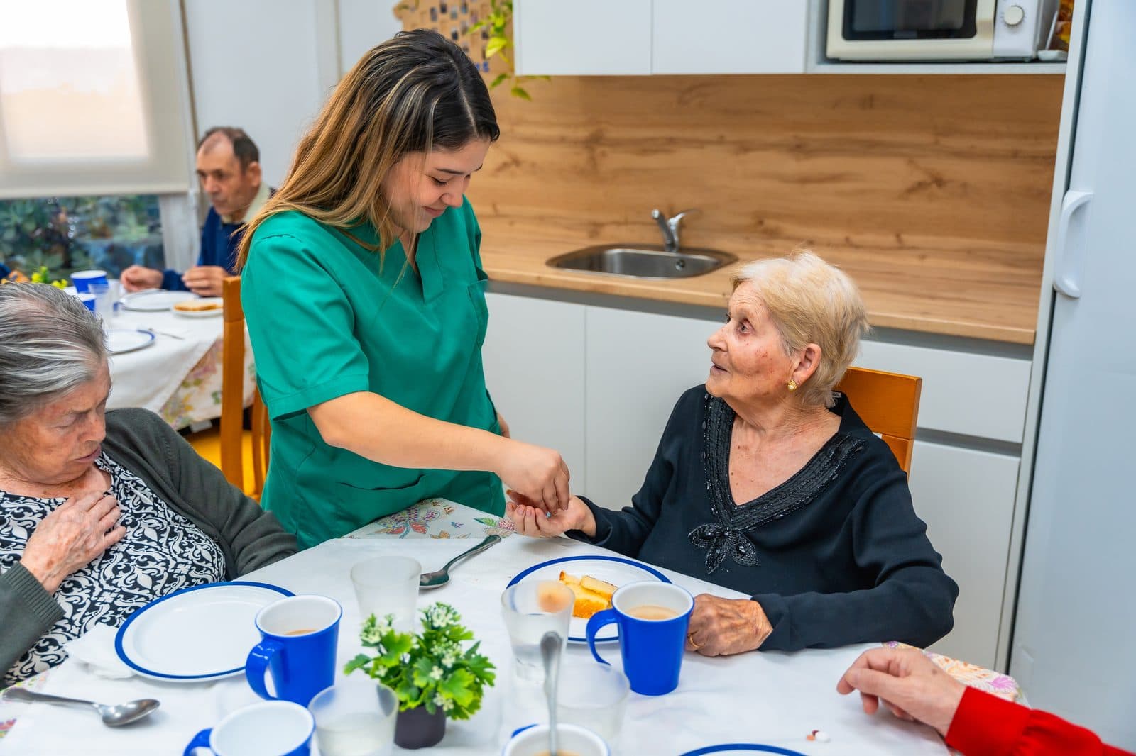 Cuidadora sirviendo la comida a una señora mayor sentada a la mesa
